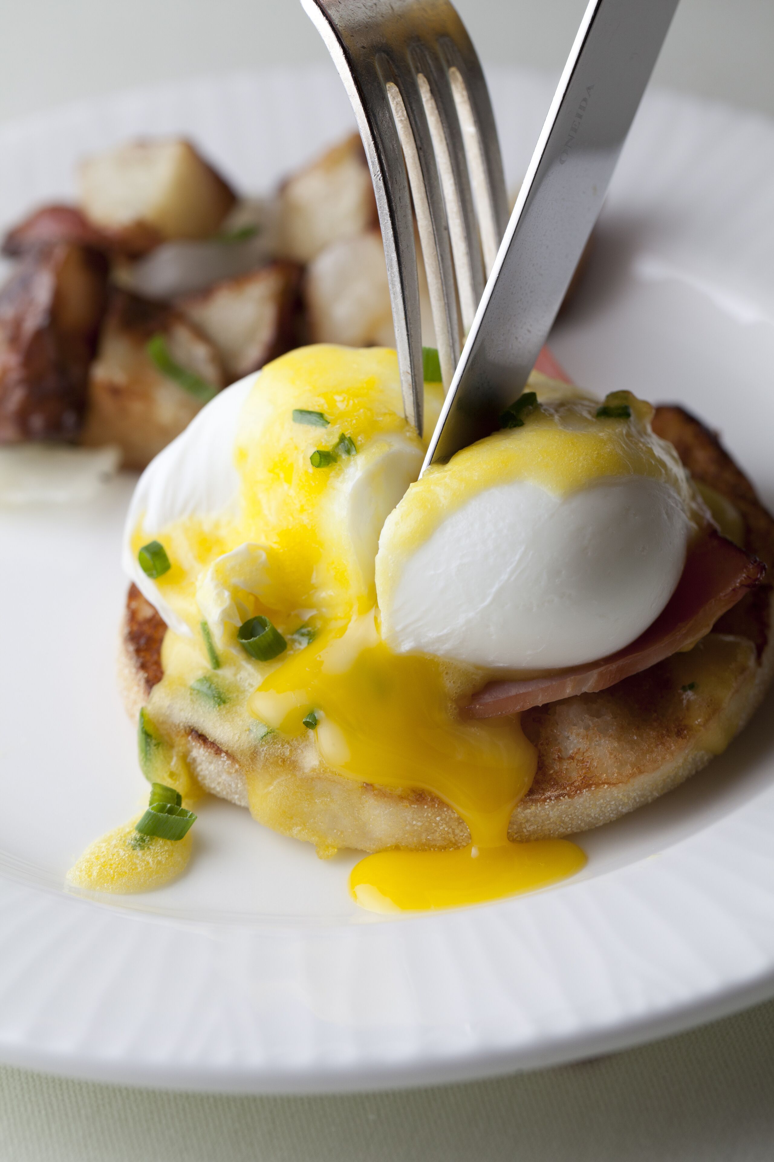 A breakfast dish with poached eggs, hollandaise sauce, and bacon on a white plate.