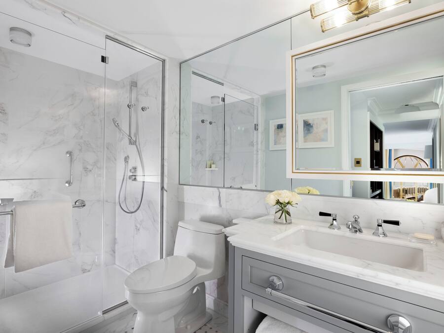 Un baño moderno con ducha de vidrio, inodoro, tocador con lavabo y un espejo grande.