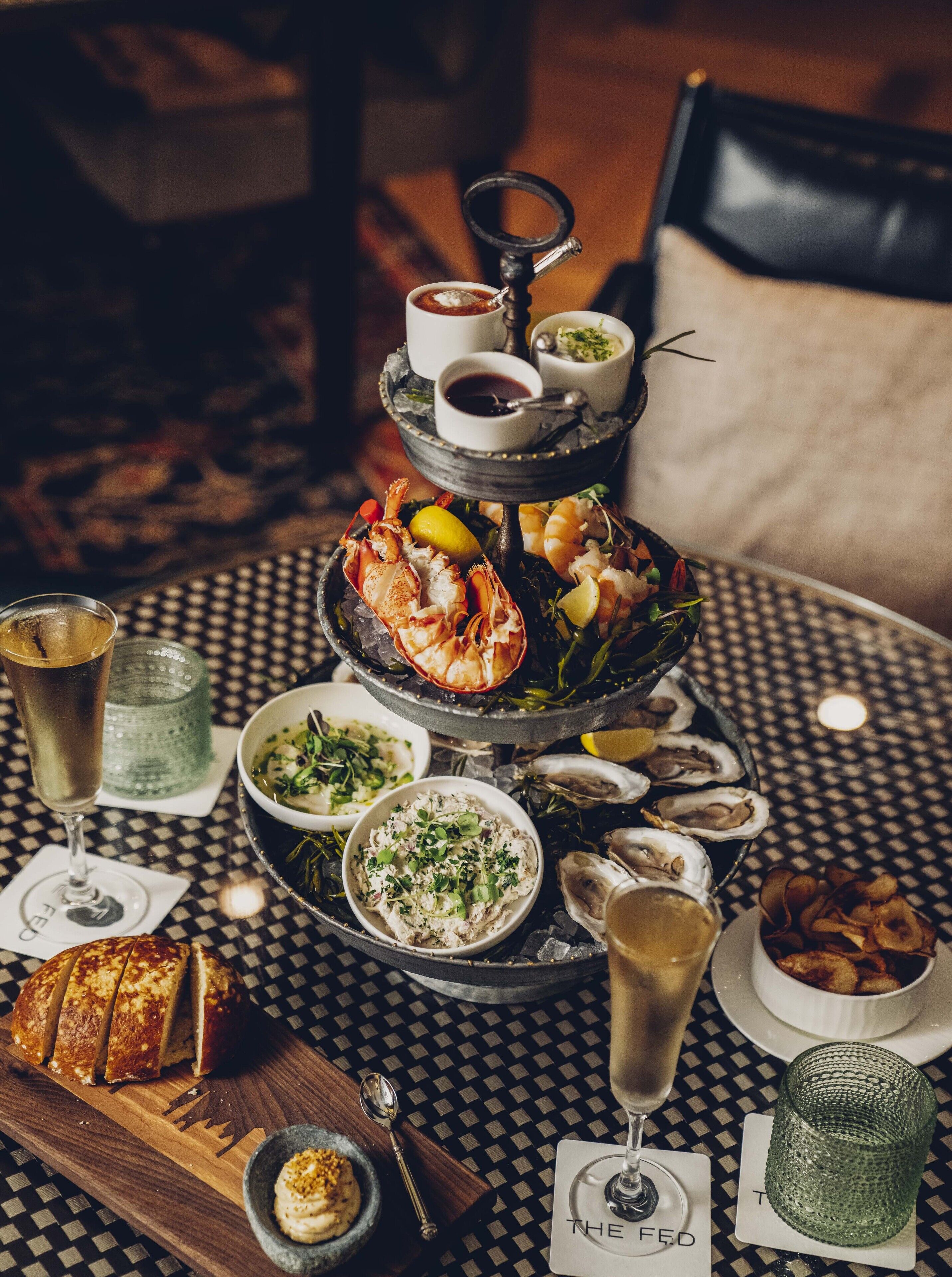 A multi-tiered seafood platter with various dishes and drinks on a checkered tablecloth.