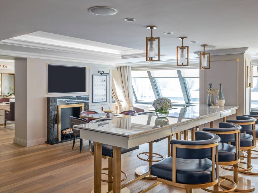 A modern dining area with a glass-top table, bar stools, and pendant lighting.