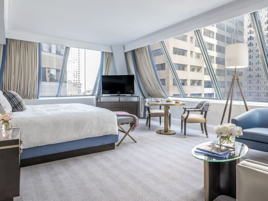 A modern hotel room with a large bed, a TV, a desk, and a view of the cityscape.
