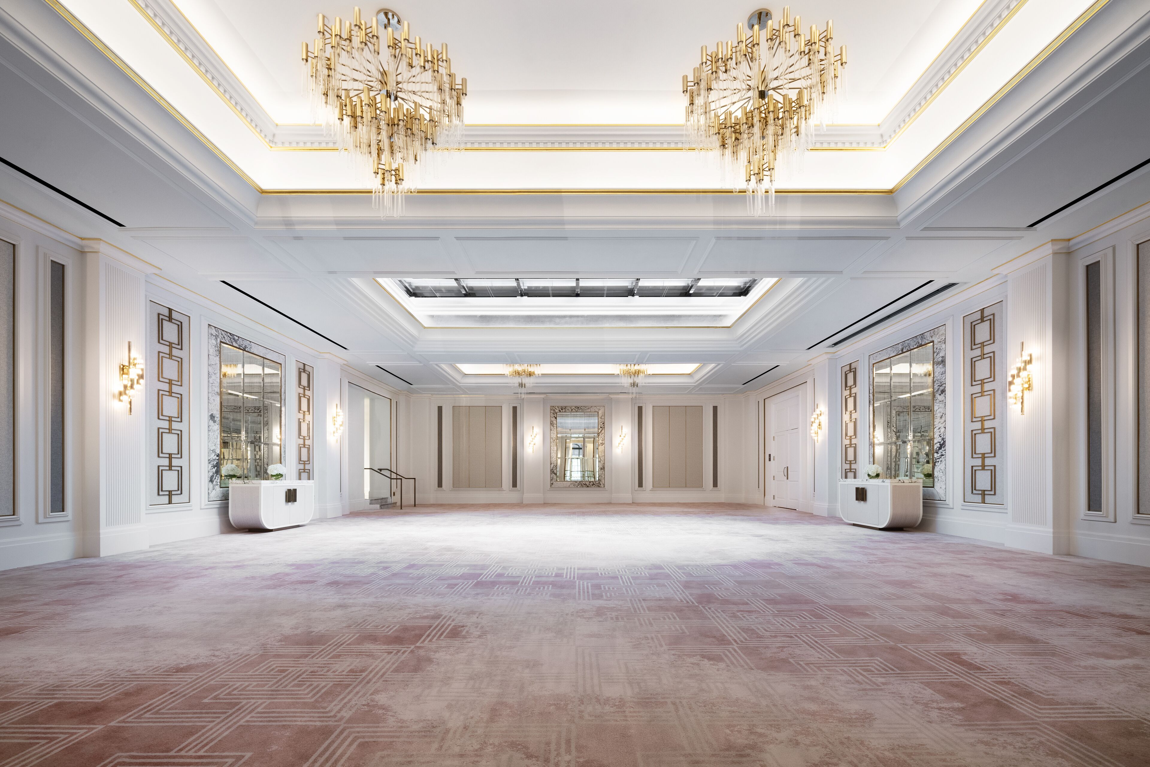 A spacious, well-lit hall with a high ceiling, chandeliers, and symmetrical wall designs.