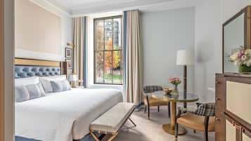 A hotel room with a large bed, a bench, a round table with chairs, a desk, and a mirror.