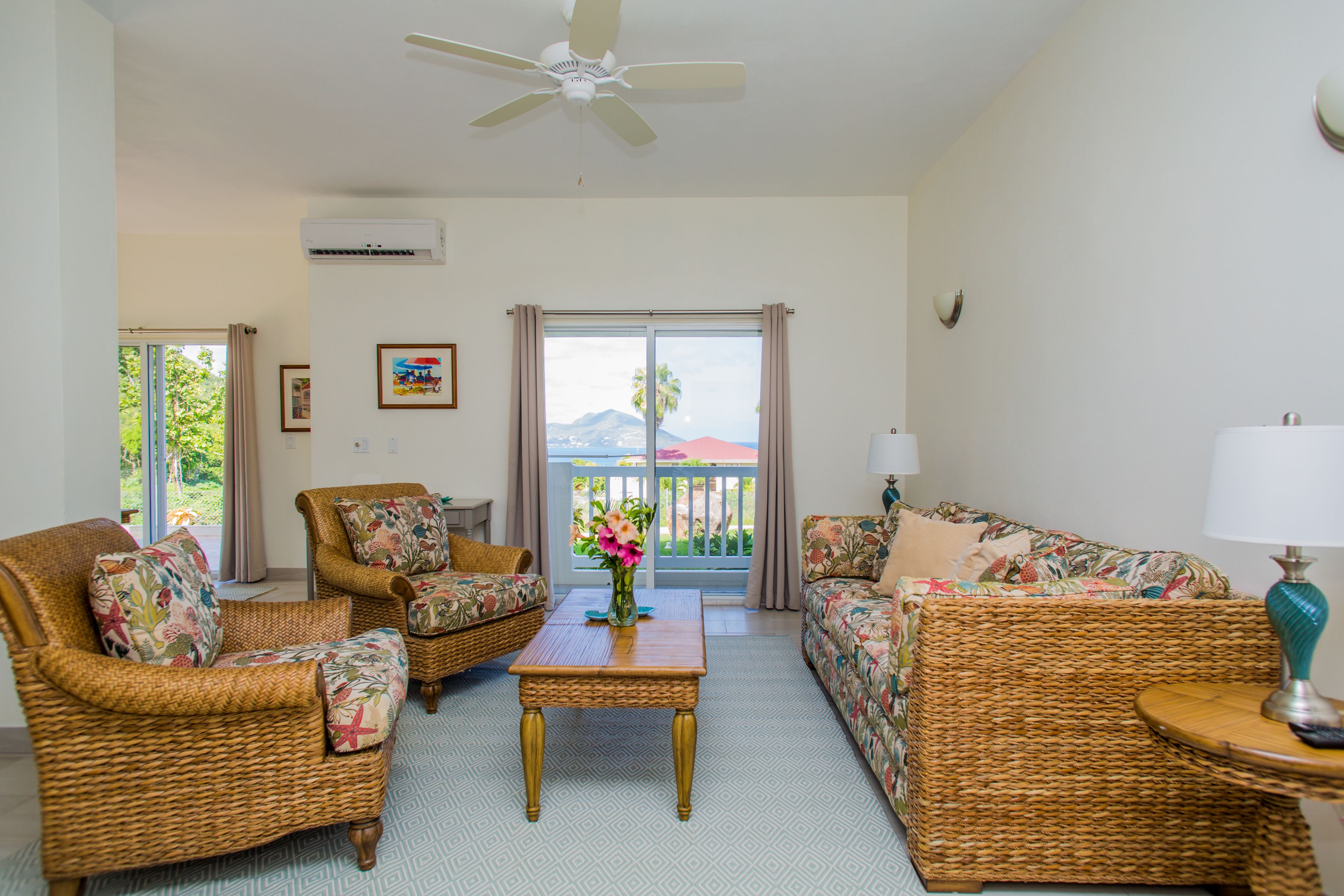 A living room with wicker furniture, a ceiling fan, and a view through a glass door.