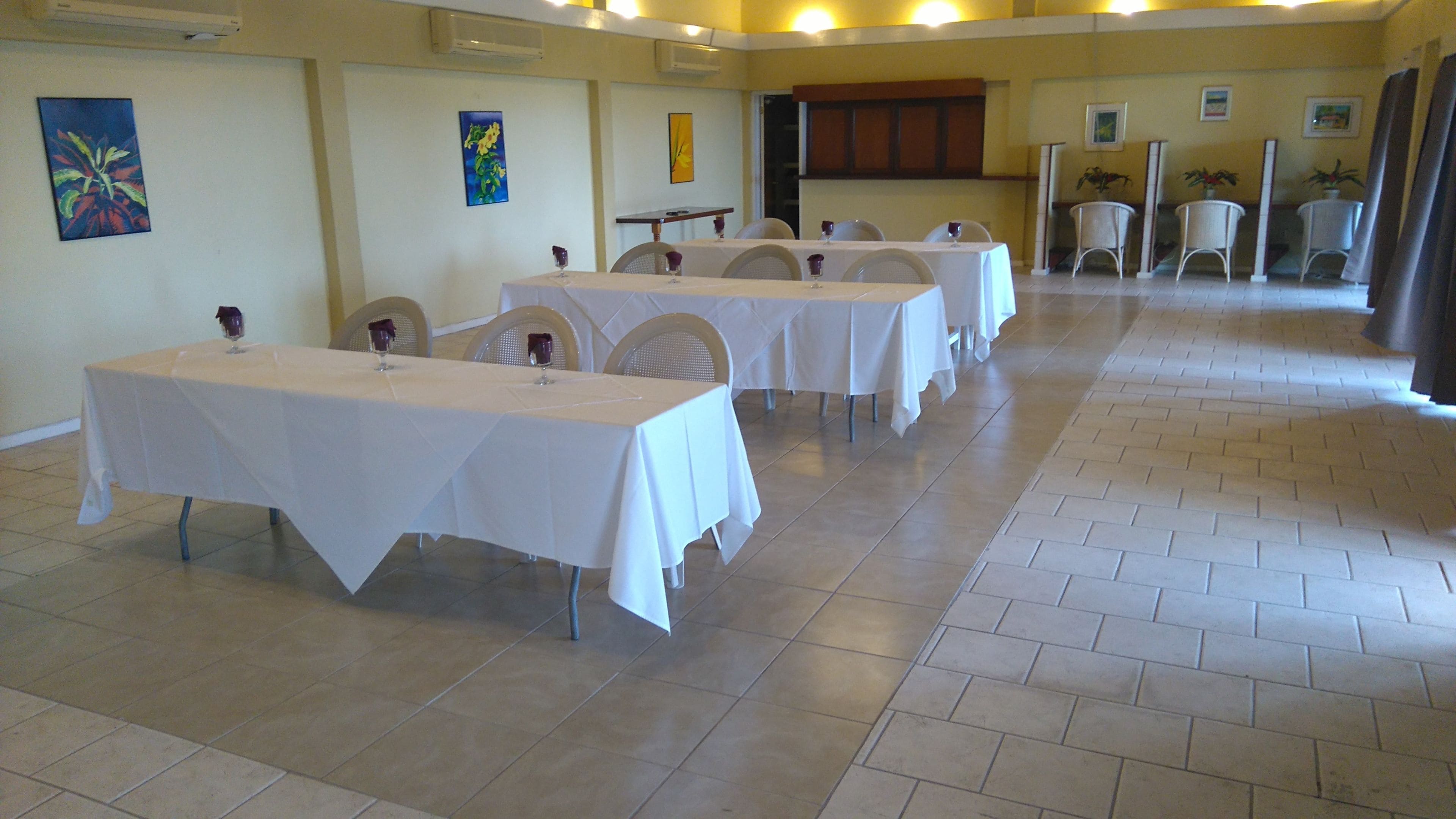Un espace repas avec plusieurs tables recouvertes de nappes blanches, des chaises et des plantes en pot.