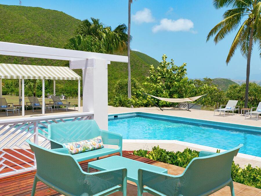 Un espace aménagé au bord de la piscine, avec deux chaises turquoise, un coin salon abrité et une vue sur la piscine et les collines.