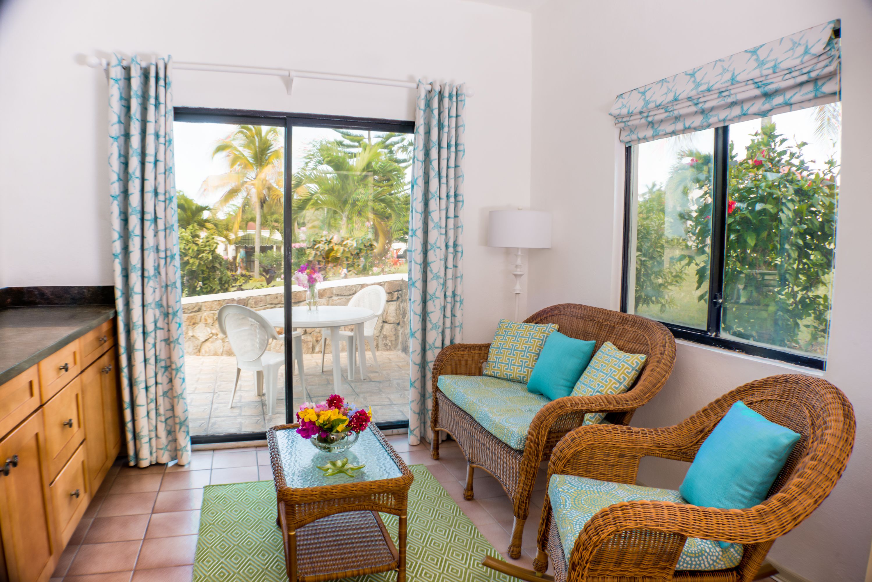Una habitación con muebles de mimbre, una mesa de comedor con sillas y vistas a palmeras a través de la puerta de cristal.