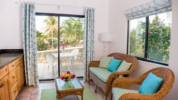 Una habitación con muebles de mimbre, una mesa de comedor con sillas y vistas a palmeras a través de la puerta de cristal.