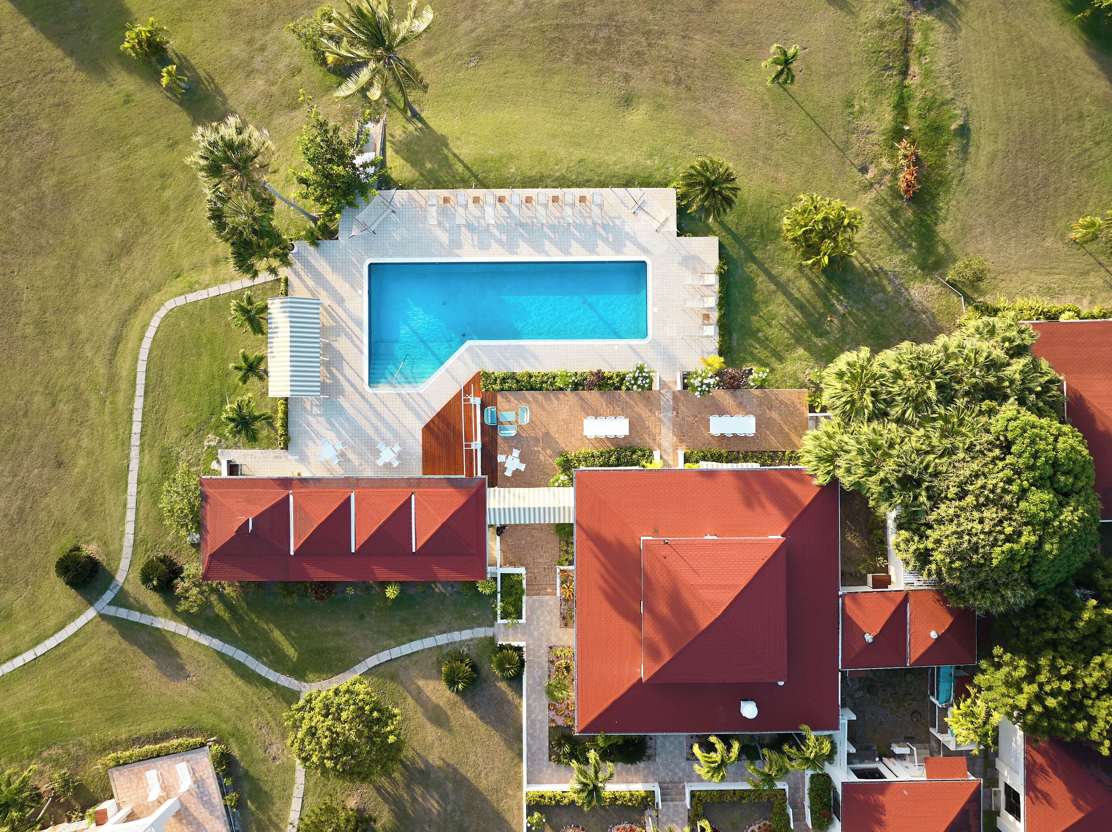 An aerial view of a property with a swimming pool, multiple buildings, and surrounding greenery.