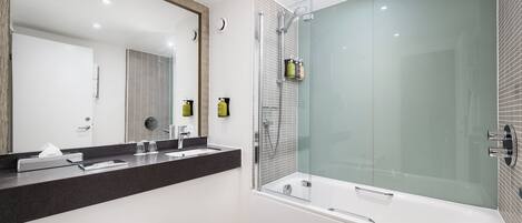 A modern bathroom with a glass-enclosed shower, a large mirror, and a black countertop with toiletries.
