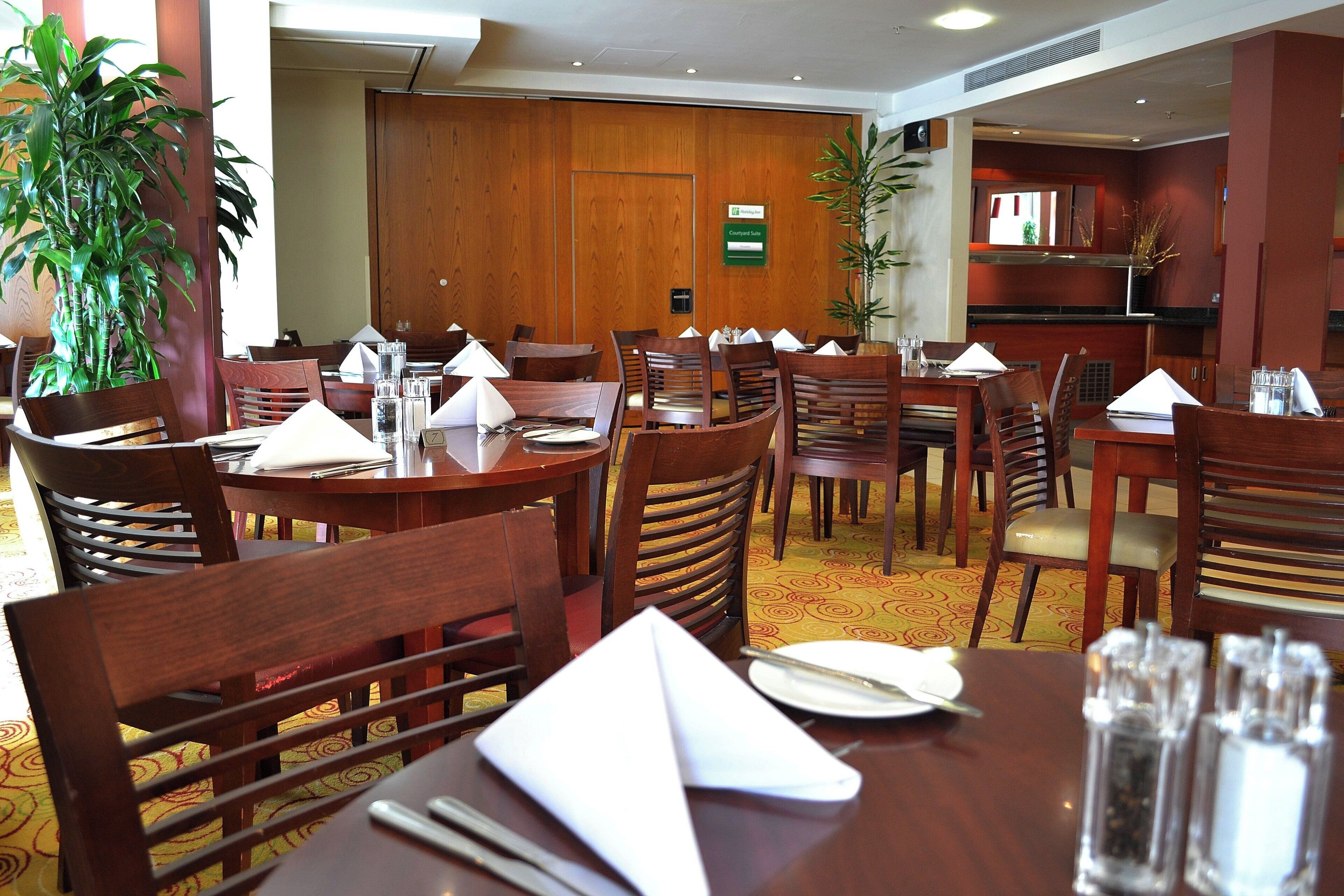 A hotel dining area with multiple tables and chairs, some with napkins and cutlery.