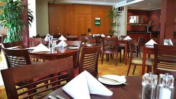 A hotel dining area with multiple tables and chairs, some with napkins and cutlery.