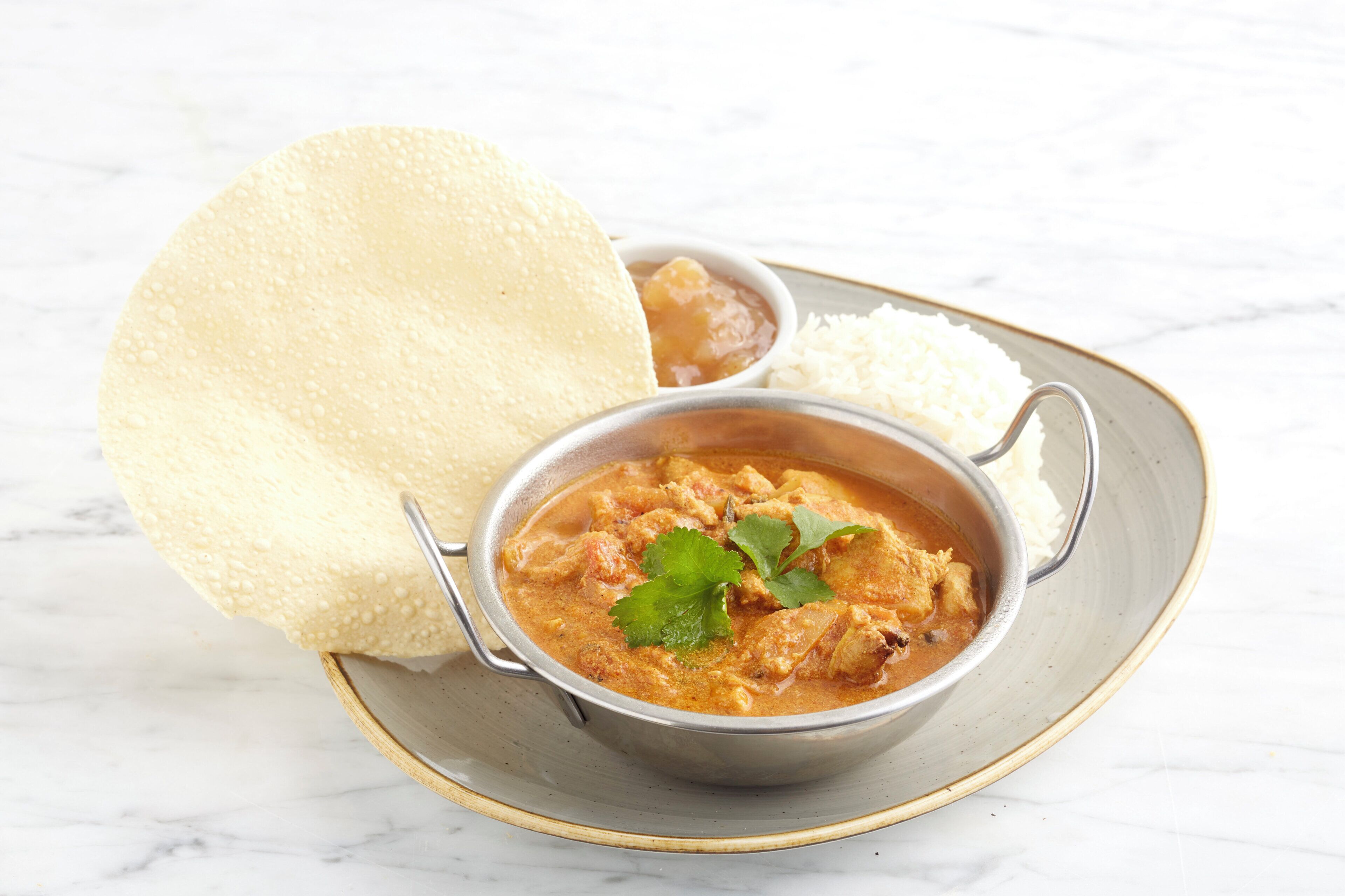 A bowl of curry with rice and a piece of bread on a plate.