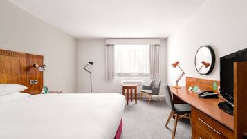 A hotel room with a bed, a desk with a computer, a chair, a lamp, and a window with curtains.