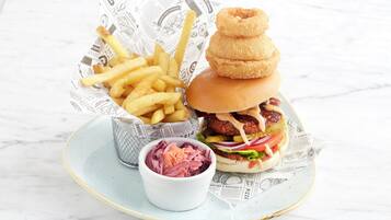 A plate with a burger, fries, onion rings, and a small bowl of coleslaw.