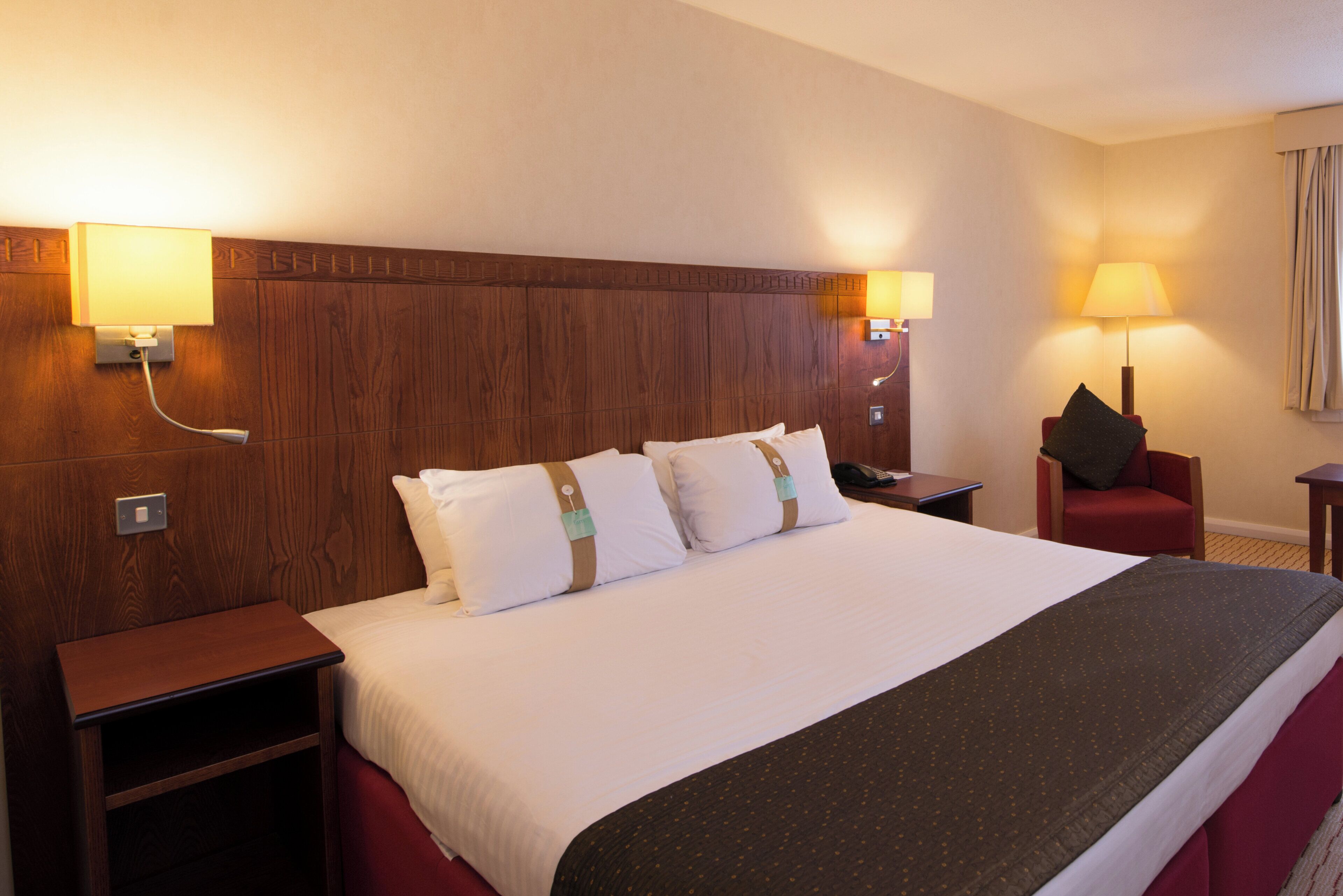 A hotel room with a large bed, two bedside tables, a red armchair, and two wall-mounted lamps.