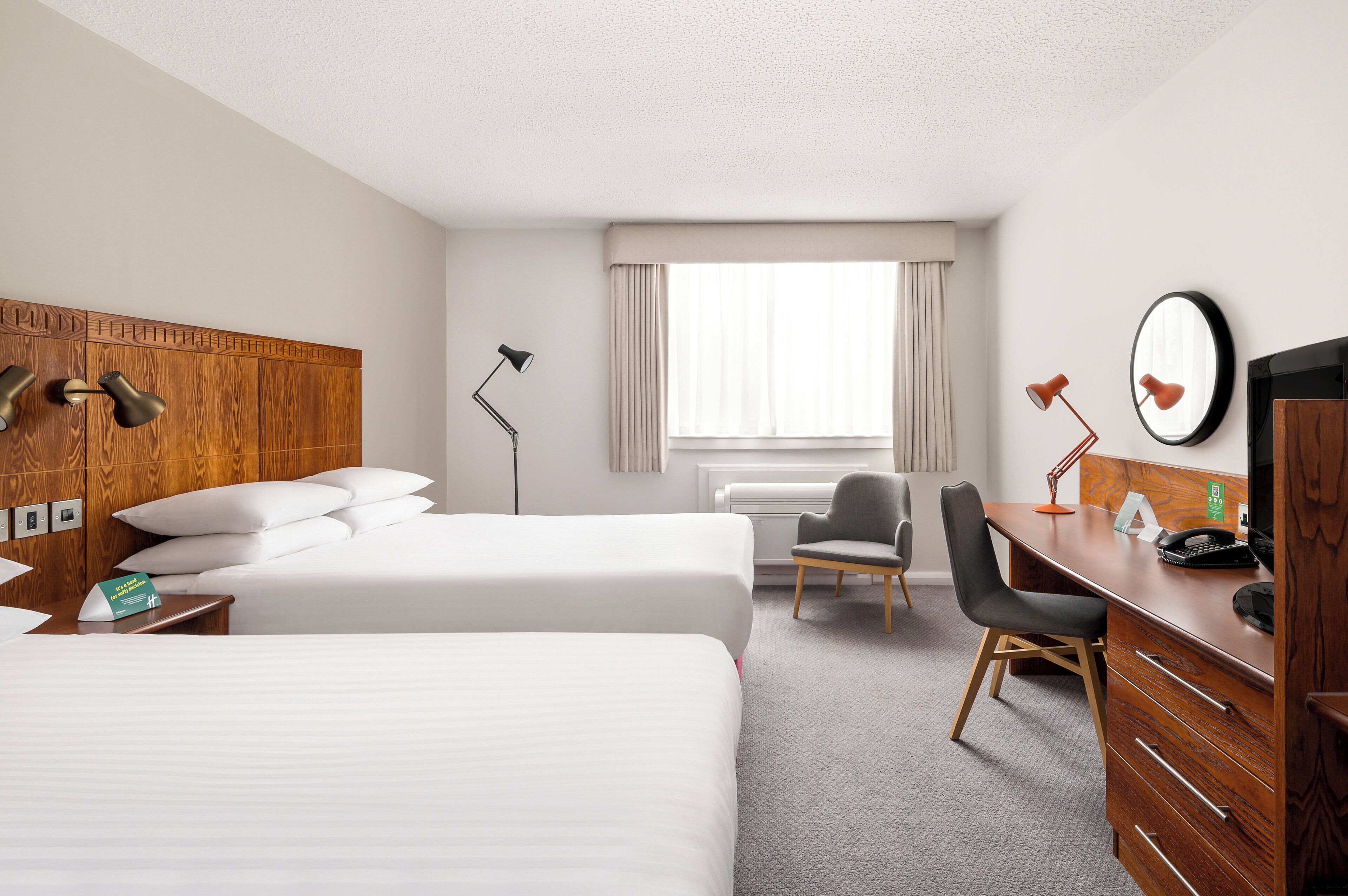 Habitación de hotel con dos camas, un escritorio con una silla, una lámpara de escritorio, un teléfono y una ventana con cortinas.