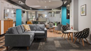 A modern interior with a grey sectional sofa, a round table with chairs, and a blue accent wall. - Holiday Inn Northampton by IHG (Northampton)