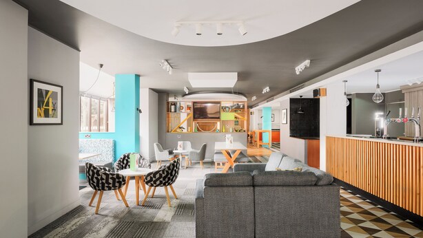 A modern interior with a dining area, a sofa, and a kitchen in the background. - Holiday Inn Northampton by IHG (Northampton)