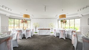 A wedding reception room with white tables, chairs, and floral centerpieces. - Holiday Inn Northampton by IHG (Northampton)