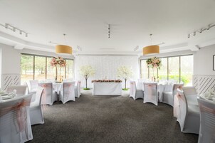 Un salón para recepción de bodas con mesas y sillas blancas, y centros de mesa florales.