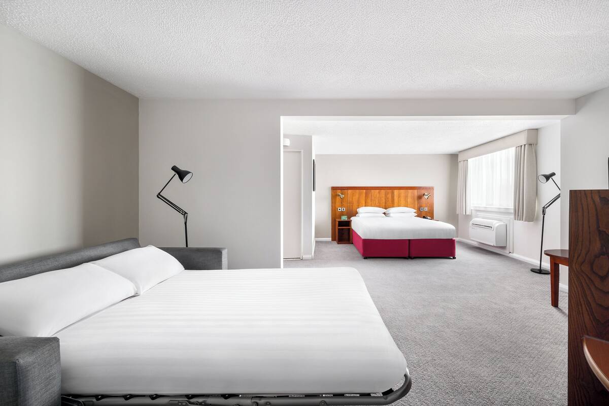 Una habitación de hotel con una cama grande, una mesita de noche, una lámpara, un armario y una ventana con cortinas.