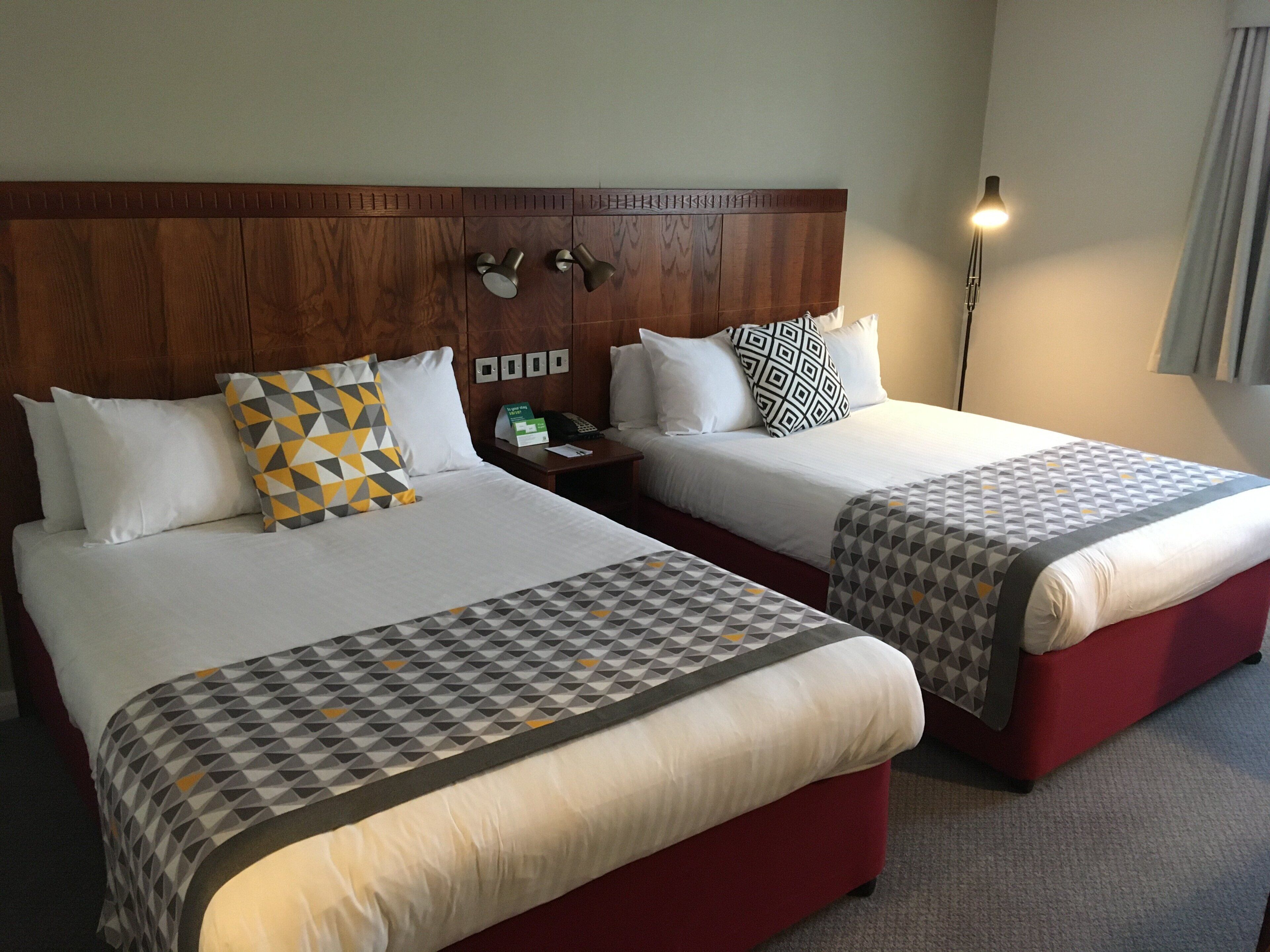 A hotel room with two beds, each with a patterned bedspread, a wooden headboard, bedside tables with lamps, and a nightstand with a telephone.