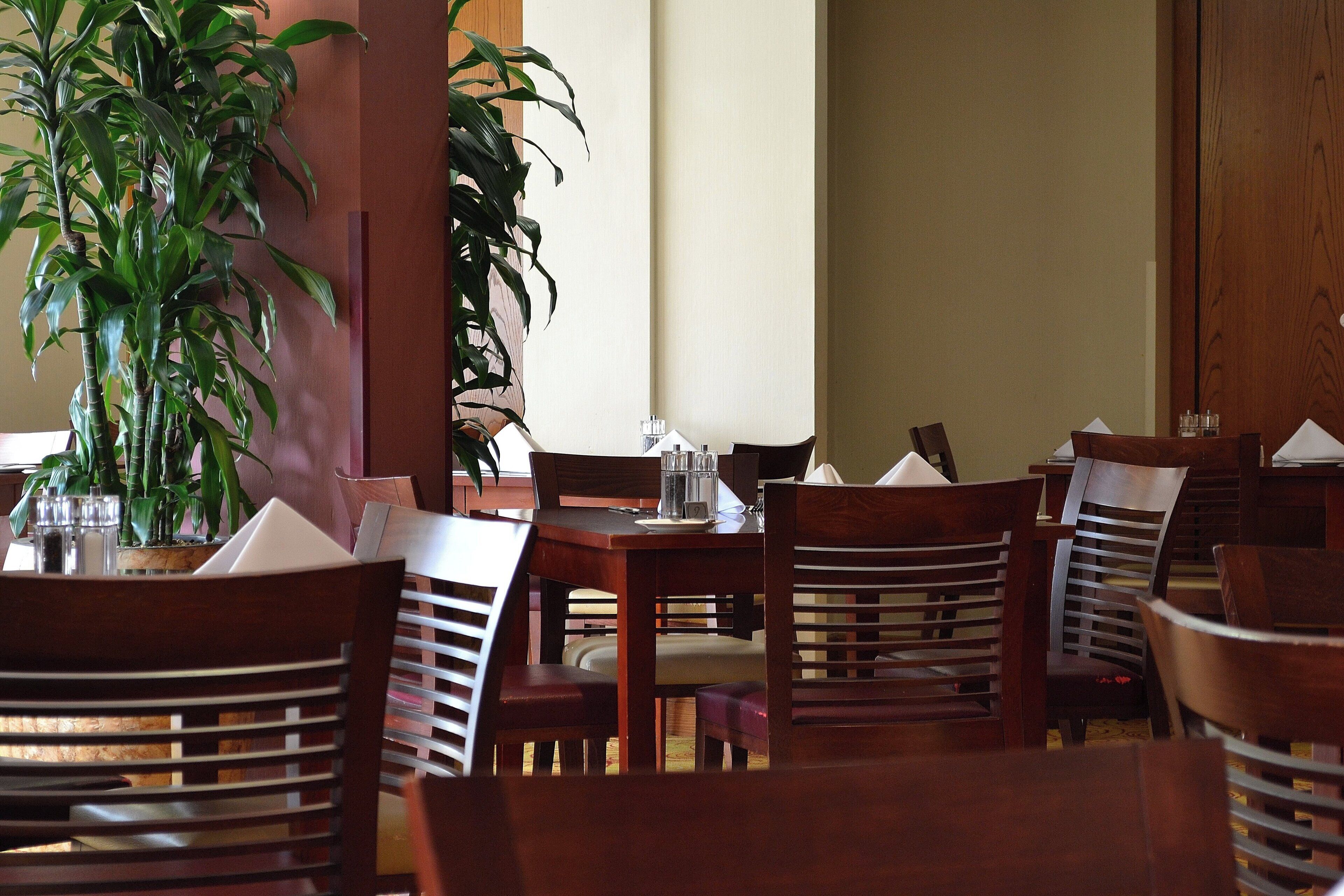 A dining area with wooden tables and chairs, a potted plant, and a wooden door in the background.