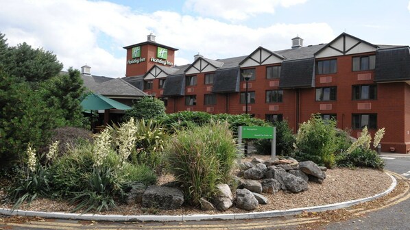 A Holiday Inn hotel with a reception sign, a garden with rocks and plants, and a building with a brick facade and a green awning.