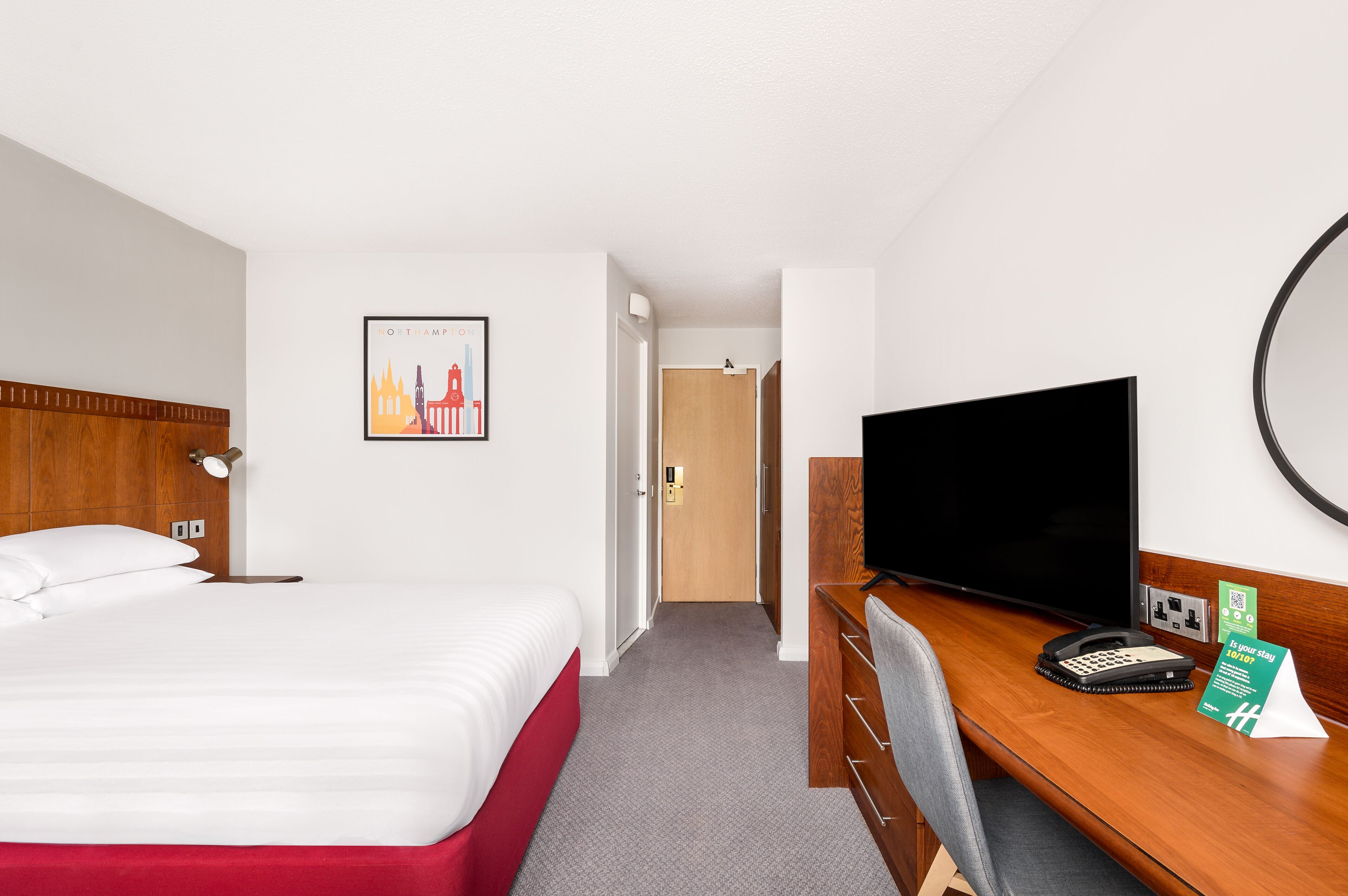 Habitación de hotel con cama, escritorio con computadora, televisor y puerta que da a otra habitación.