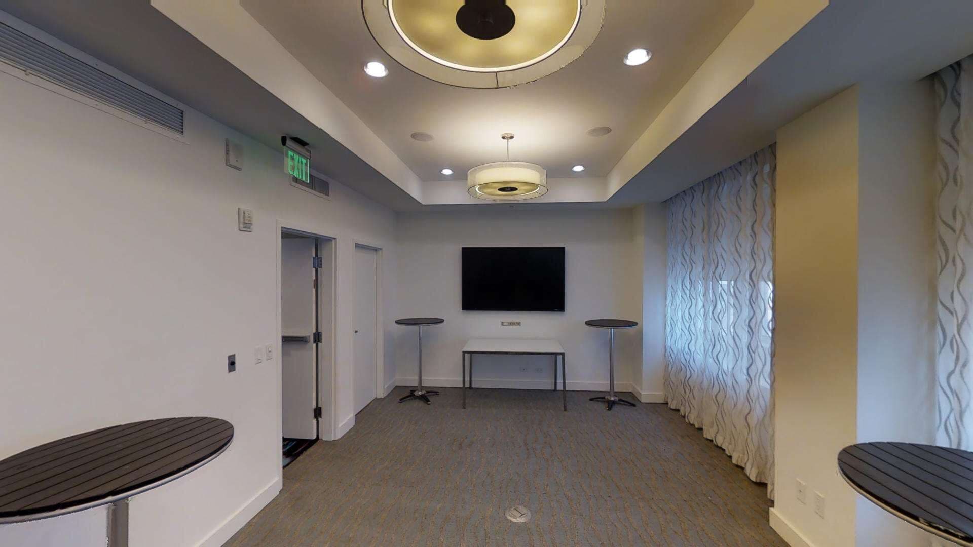 A conference room with a flat-screen TV, two small tables, and a ceiling light fixture.