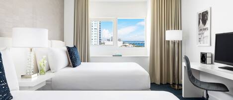 A hotel room with two beds, a desk with a computer, a chair, and a view of the cityscape.