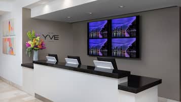 A hotel reception desk with a cityscape view on the wall, a vase of flowers, and a sign reading "YVE Miami".