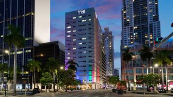 A modern hotel with a prominent 'YIVE Miami' sign, surrounded by palm trees and other buildings.
