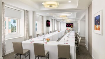 A hotel conference room with a long table, chairs, and a digital display.