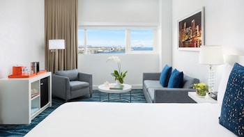 A modern hotel room with a grey sofa, a small round coffee table, a bookshelf, and a large window with a cityscape view. at YVE Hotel Miami