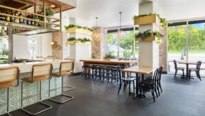 A modern restaurant with a bar area, seating, and large windows offering a view of the outdoors. - YVE Hotel Miami (Miami)
