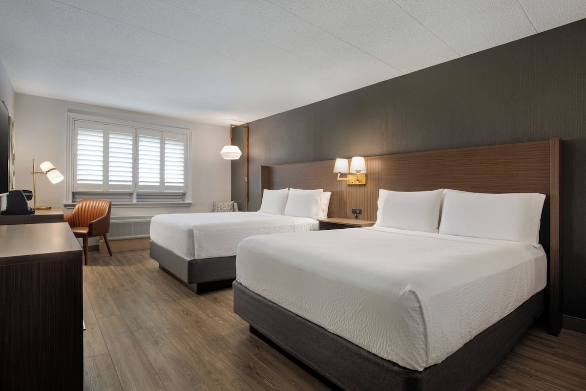 Habitación de hotel con dos camas, un escritorio, una silla y un ventanal con persianas.