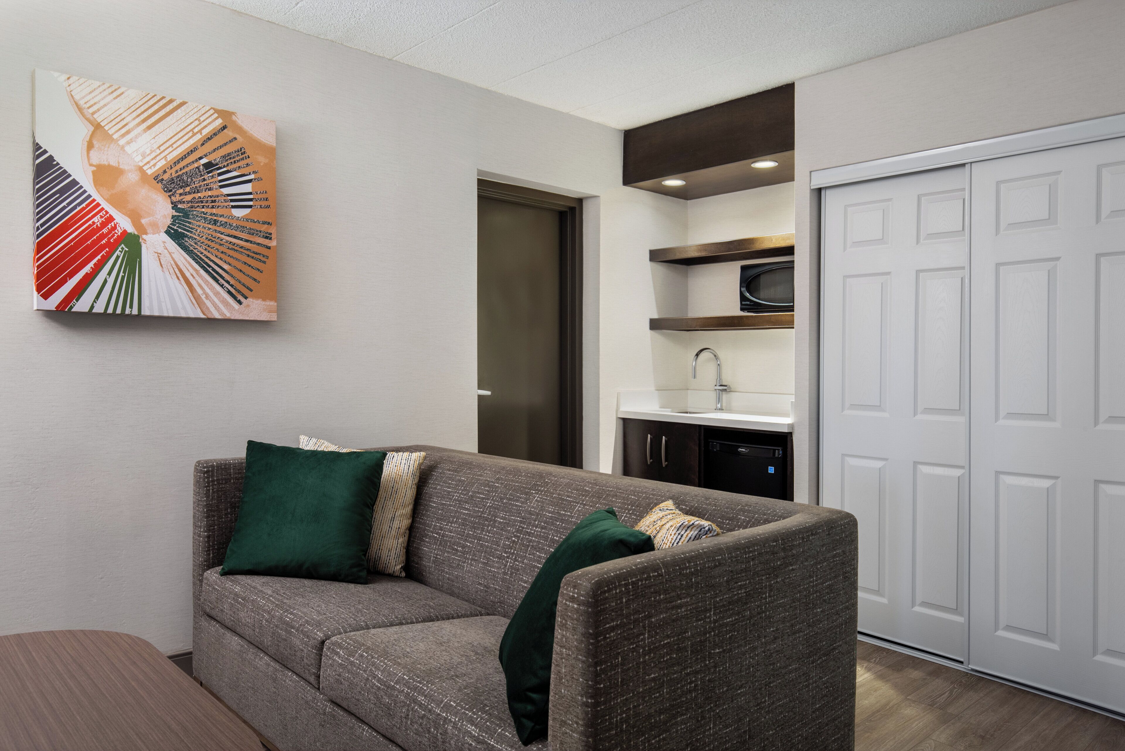 A modern living room with a grey sofa, a green throw pillow, and a wall-mounted abstract art piece.