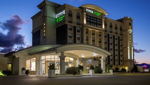 A large hotel with a prominent Staybridge name, a Holiday Inn & Suites sign, and a well-lit entrance with a covered walkway.