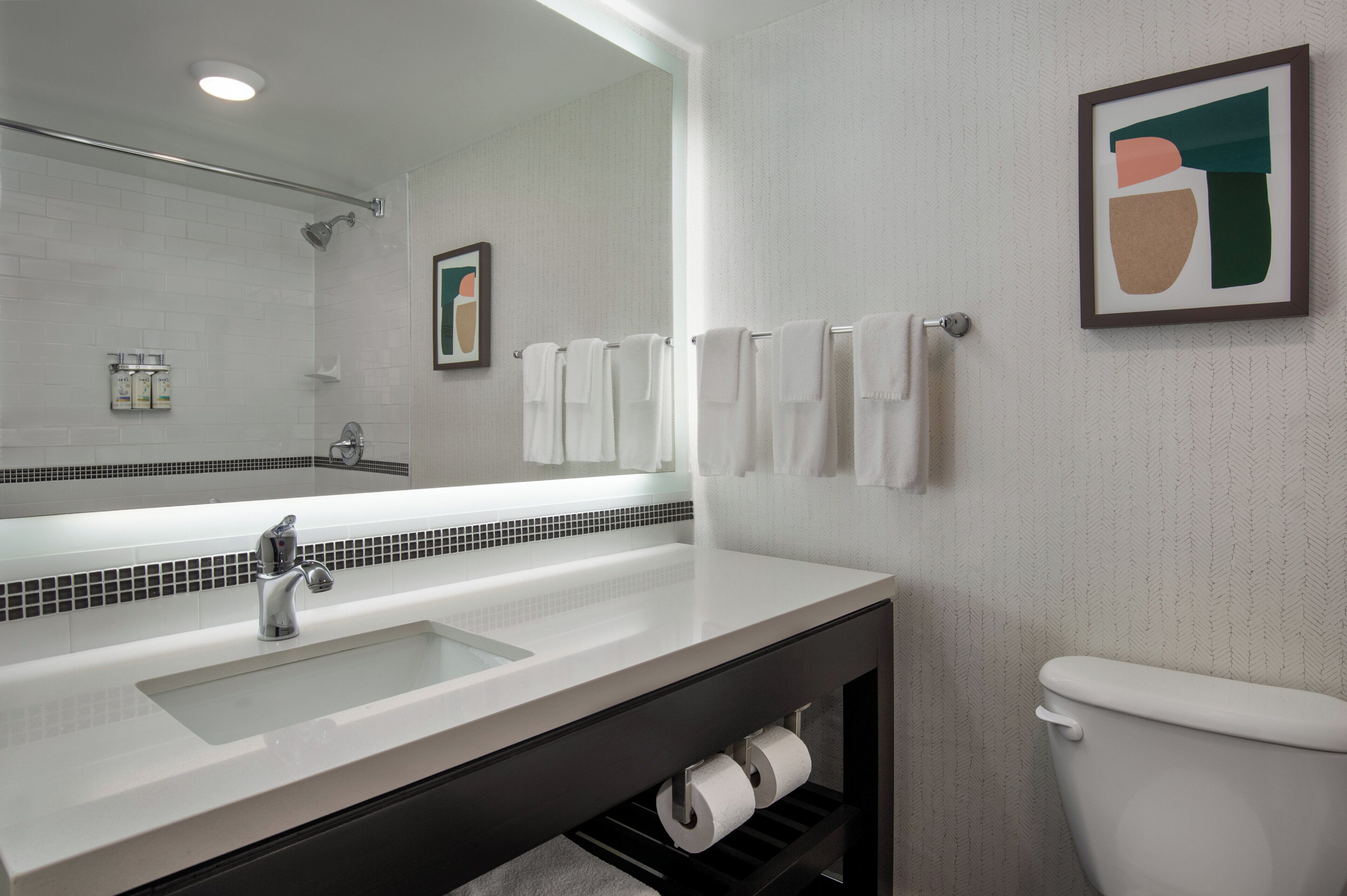 A modern bathroom with a large mirror, white sink, and toilet.