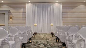 A formal event space with rows of white-covered chairs, a draped backdrop, and lanterns on a patterned carpet.