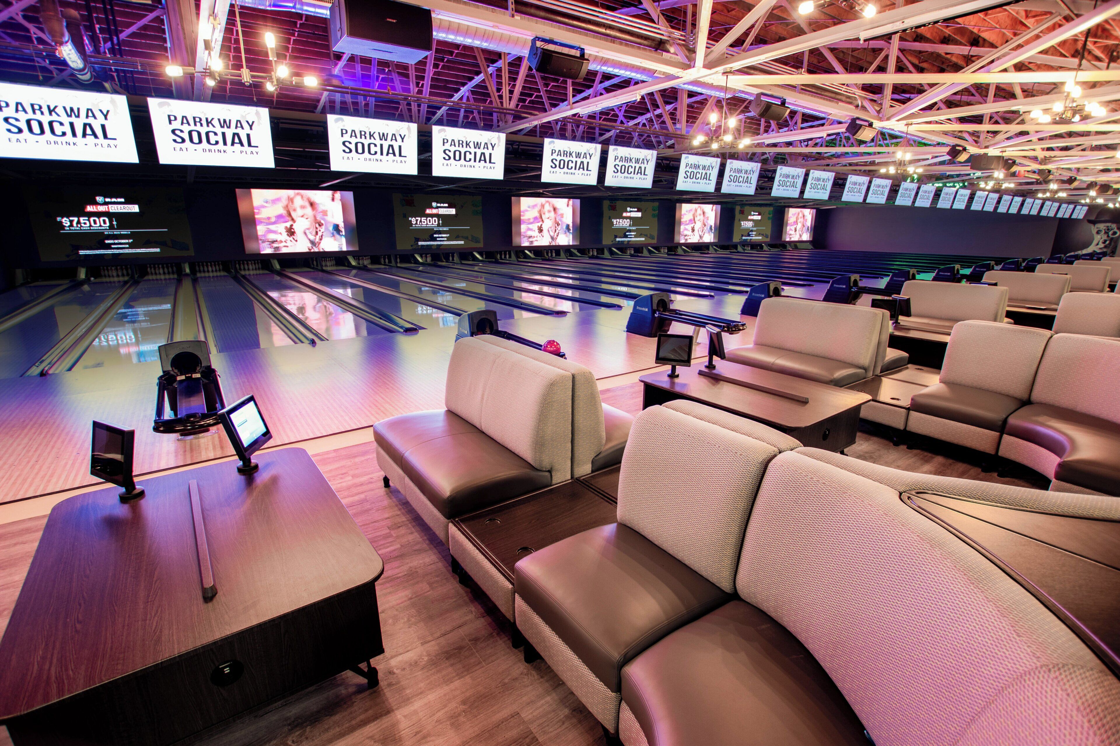 A bowling alley with multiple lanes, seating areas, and overhead signage.