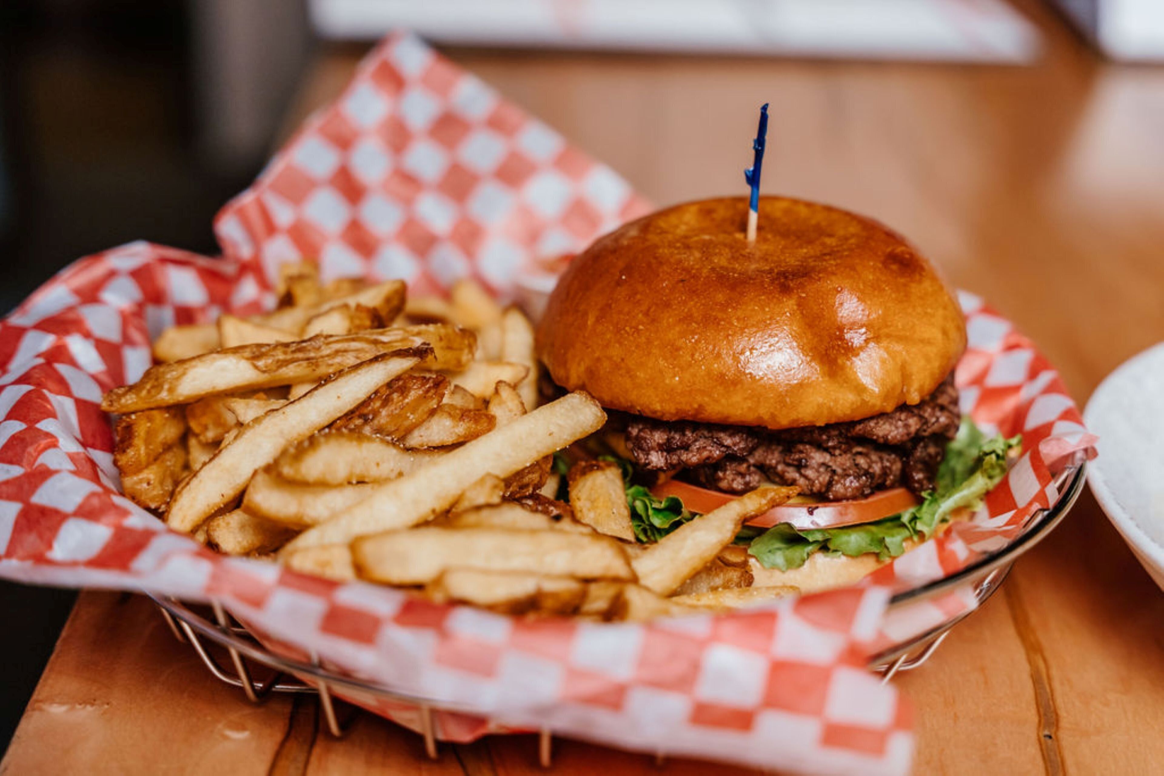 A burger with a bun and a toothpick, accompanied by a basket of fries.