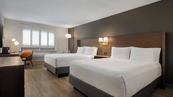 Une chambre d’hôtel avec deux lits, un bureau, une chaise et une grande fenêtre avec des stores.