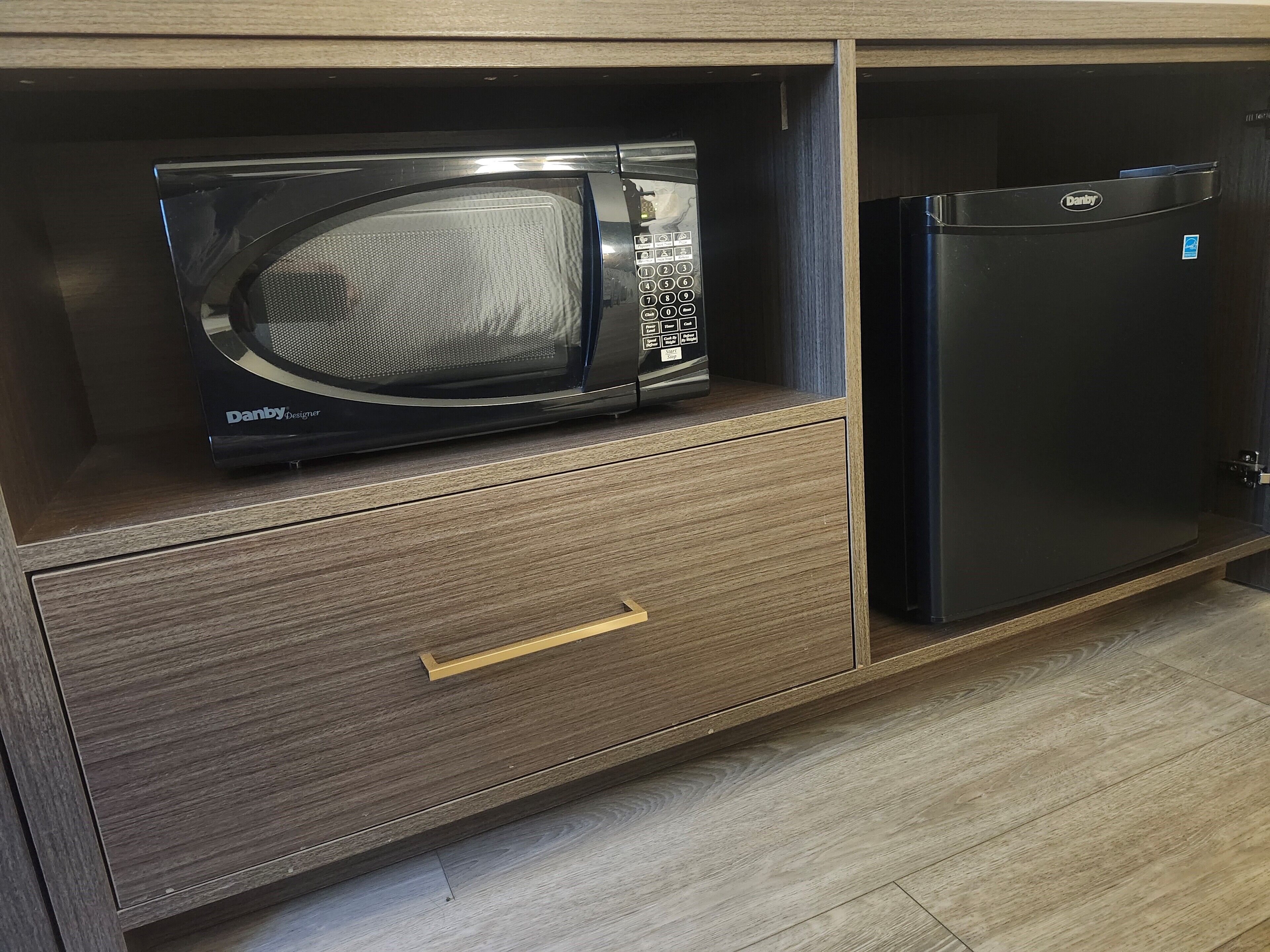 Un microondas y un refrigerador en una cocina con un armario y un cajón de madera.