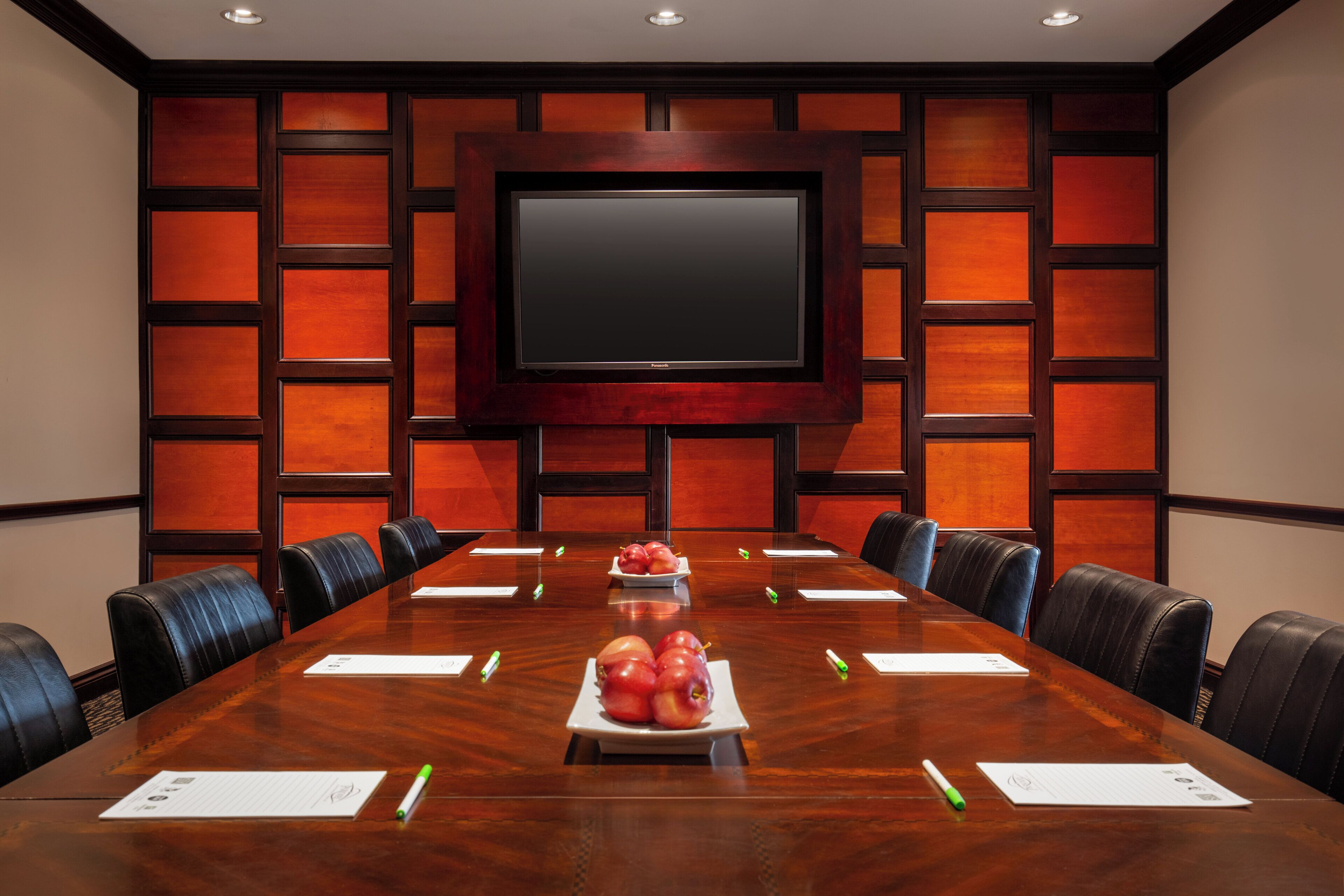 A conference room with a long table, chairs, a screen, and fruit on the table.