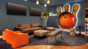 A modern living room with a bowling pin mural, a brown sofa, orange armchairs, and a wooden coffee table.