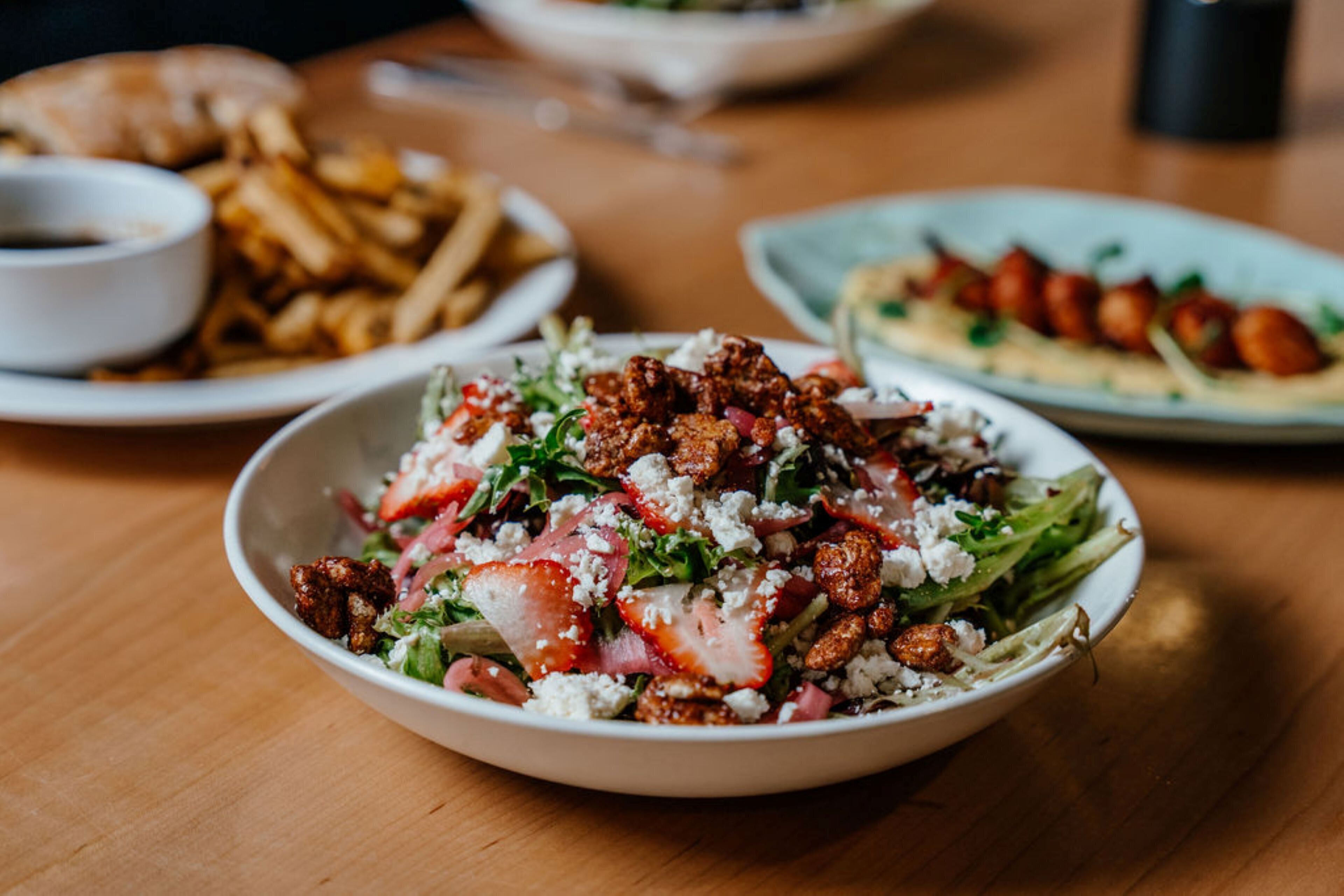 A dining table with various dishes including a salad, fries, and a plate with nuts.