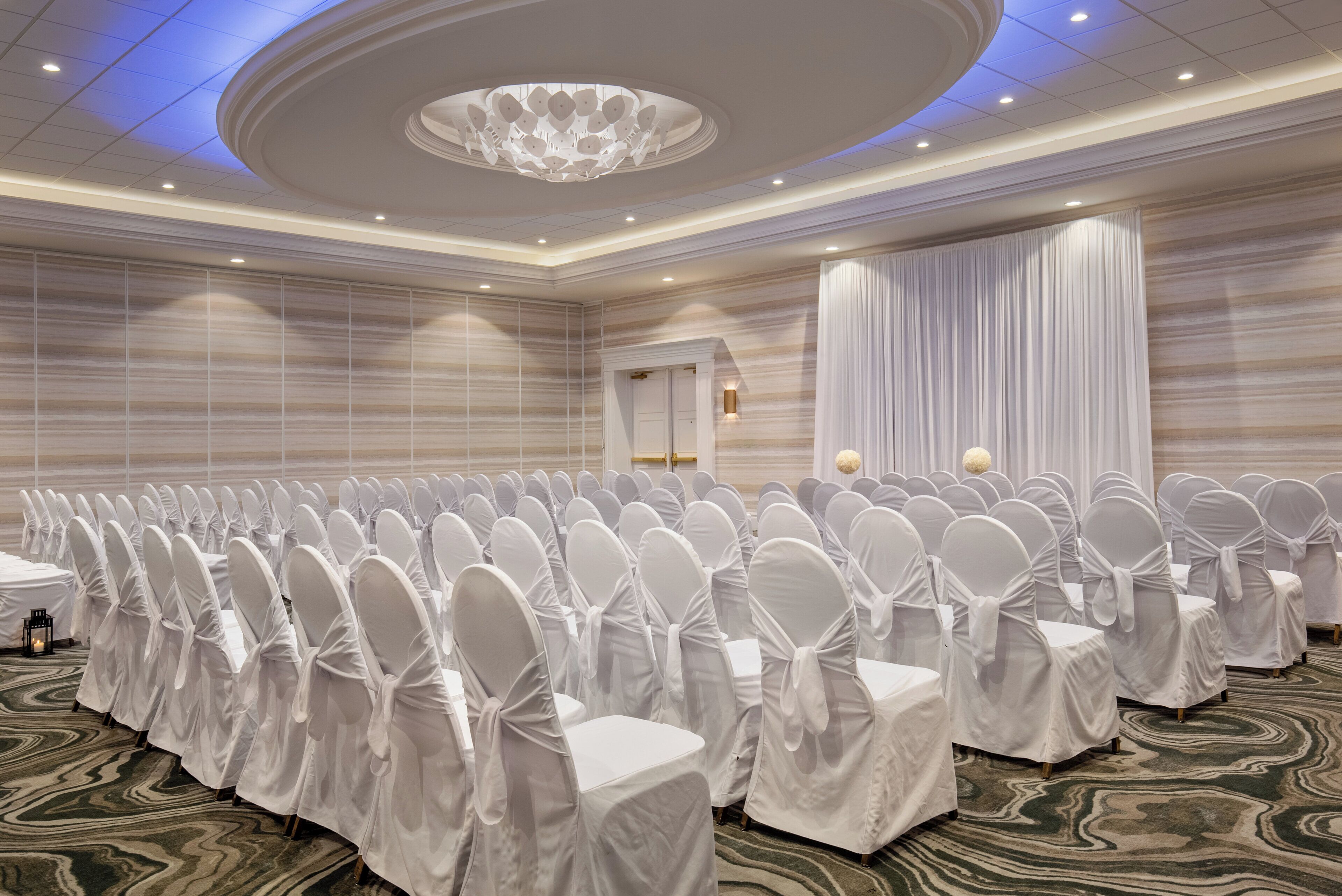 A conference room with rows of white-covered chairs, a large chandelier, and a patterned carpet.